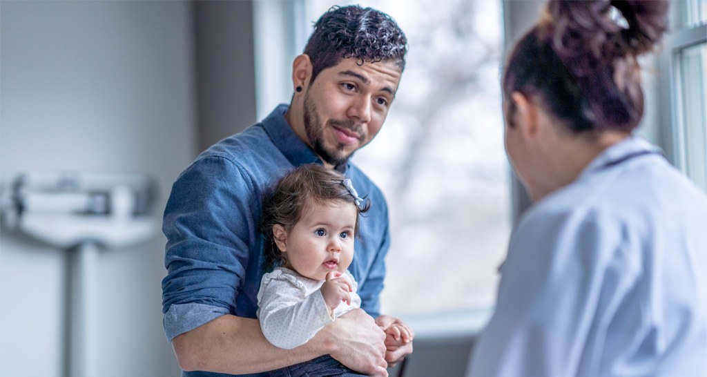 Man holding infant child while talking to female doctor. 