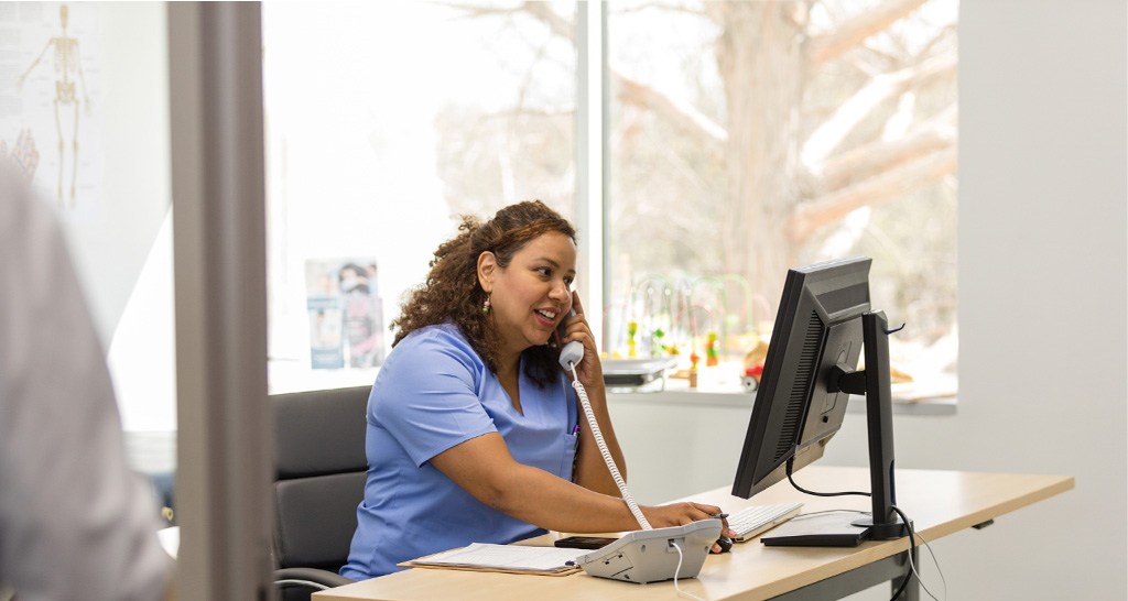 Female nurse looks at information on a computer while talking on the phone.